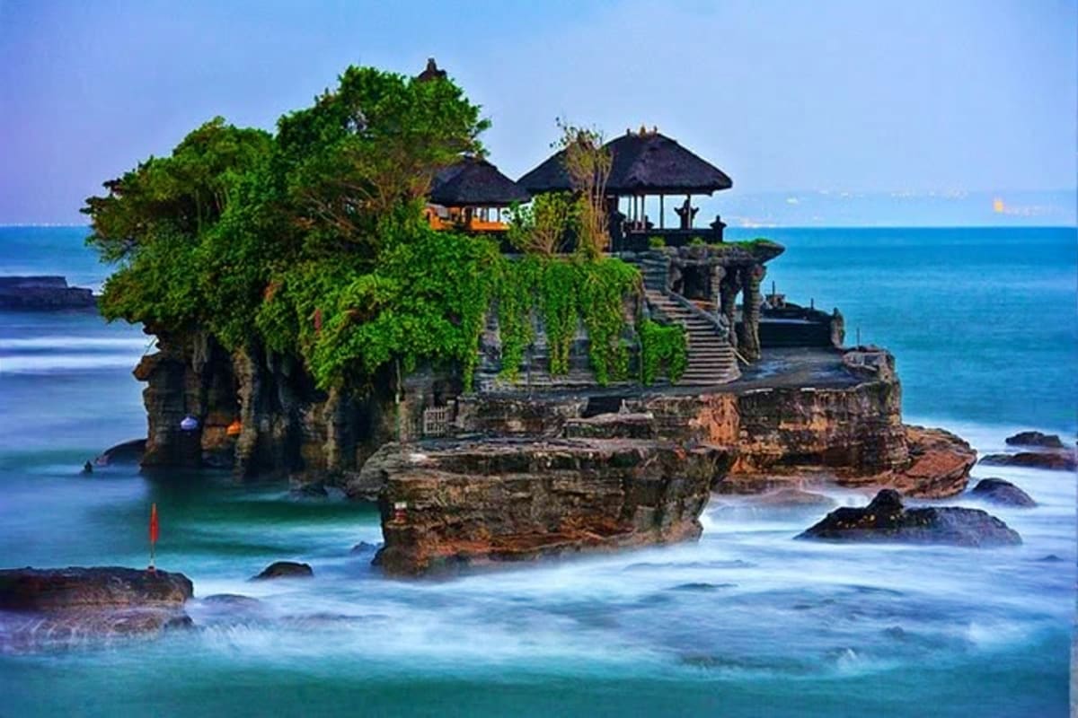 Tanah Lot temple on a rocky island surrounded by turquoise ocean waves and lush green vegetation in Bali, Indonesia