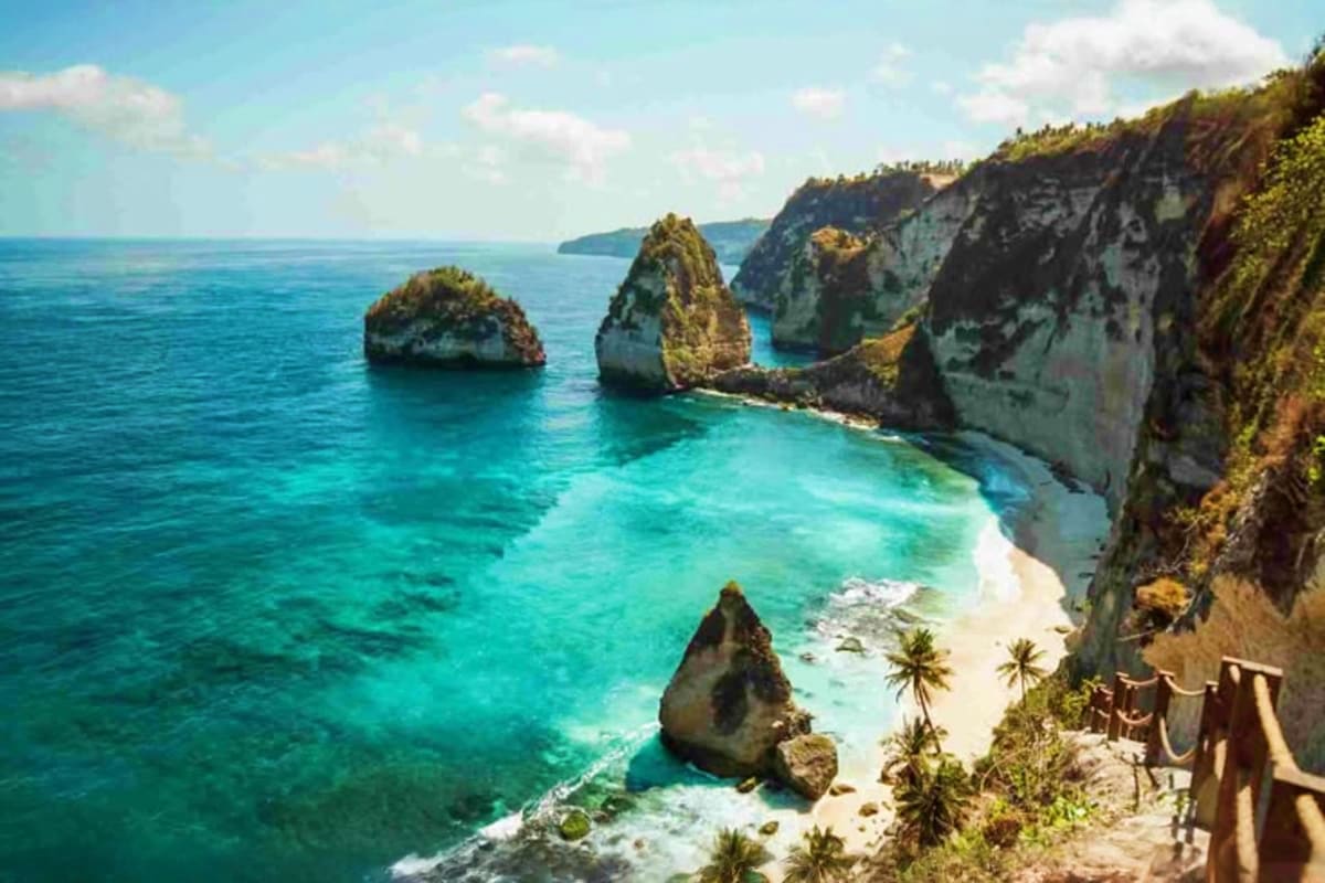 Best of Bali Aerial view of Kelingking Beach in Bali showing turquoise waters, limestone cliffs, rock formations, and white sand beach wit