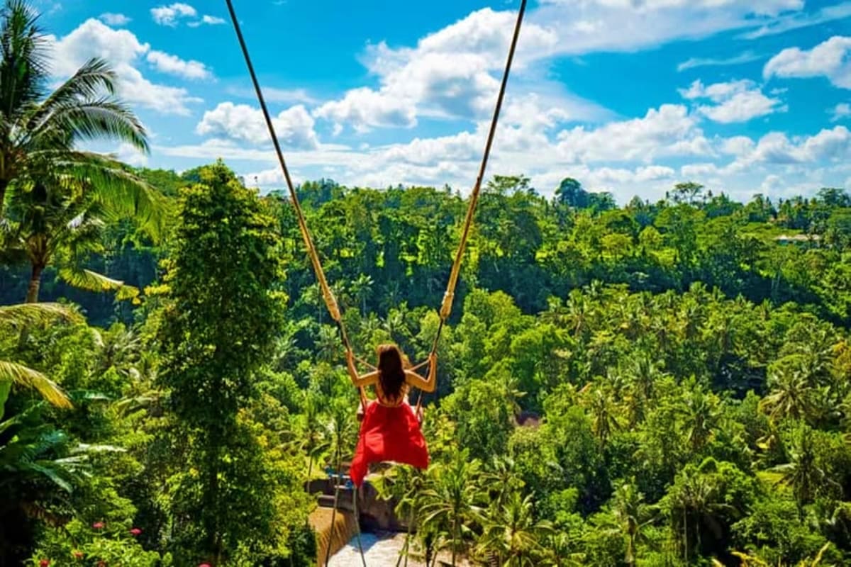 Best of Bali Woman on jungle swing in red shirt overlooking lush tropical forest canopy in Bali