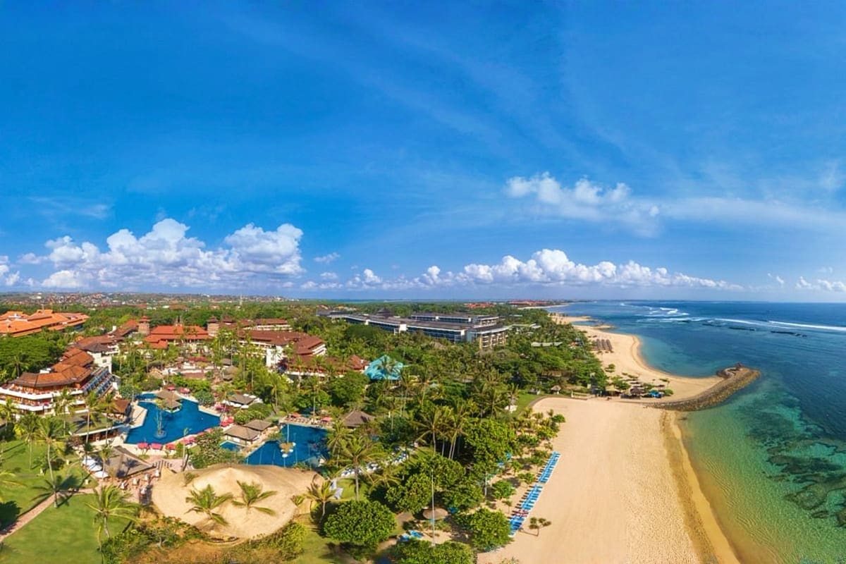 Aerial view of tropical resort with blue pools, sandy beach, and ocean in Bali