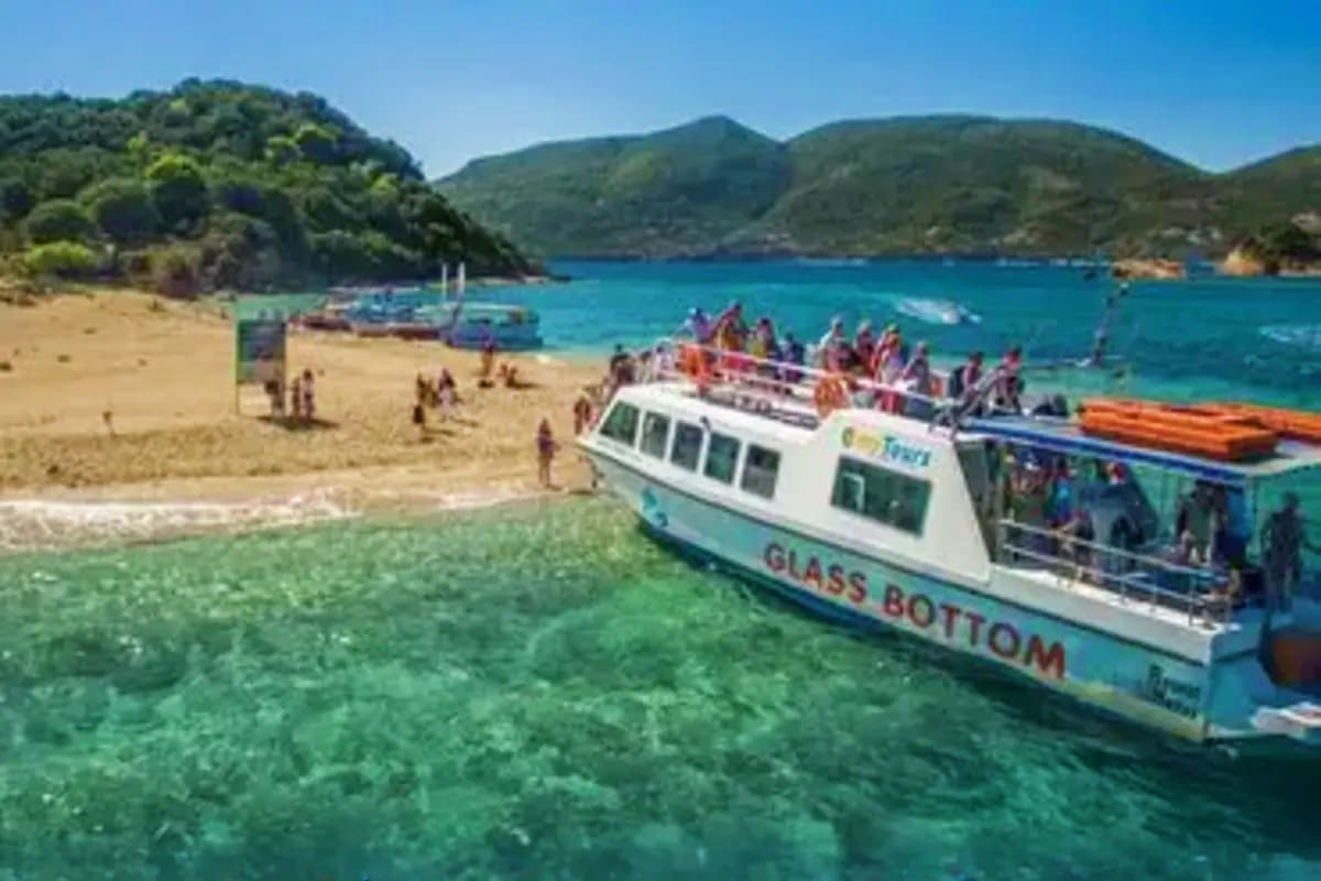 Bali Family Fun Glass bottom boat with tourists in clear turquoise water at scenic beach cove surrounded by forested hills