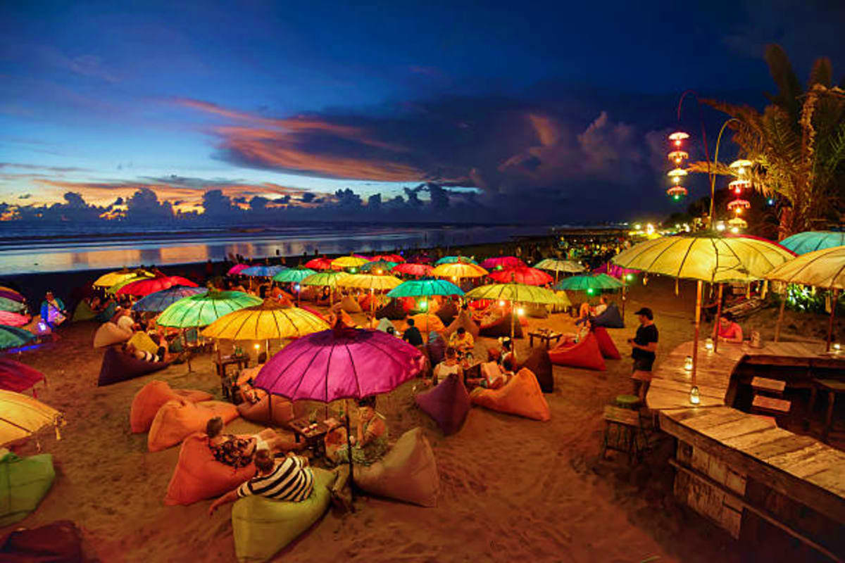Bali and Nusa Penida Island Hopper Colorful umbrellas and bean bags lighting up a Bali beach at dusk with ocean and sunset sky in background