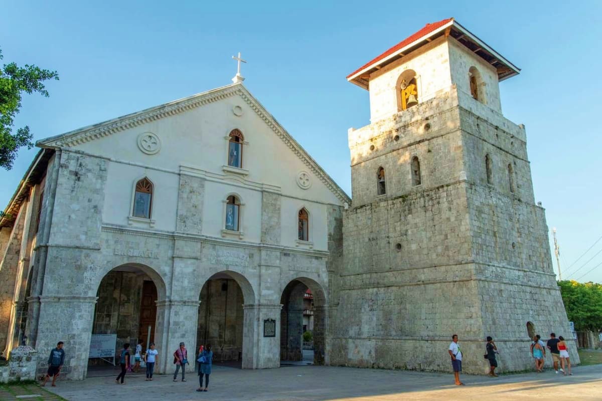 Philippines Nature and Culture Tour Historic stone church with bell tower and red-tiled roof, visitors gathered in plaza, Philippines cultural landmark