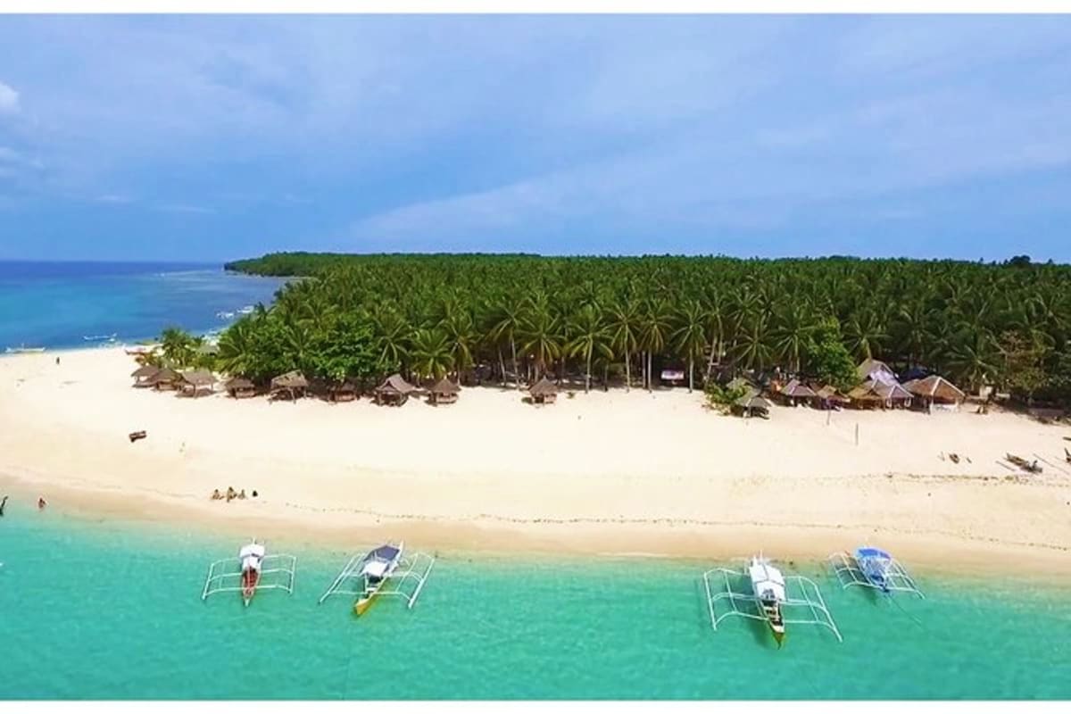 Simply Siargao Aerial view of Siargao island beach with turquoise waters, traditional outrigger boats, white sand, palm trees, and thatched-