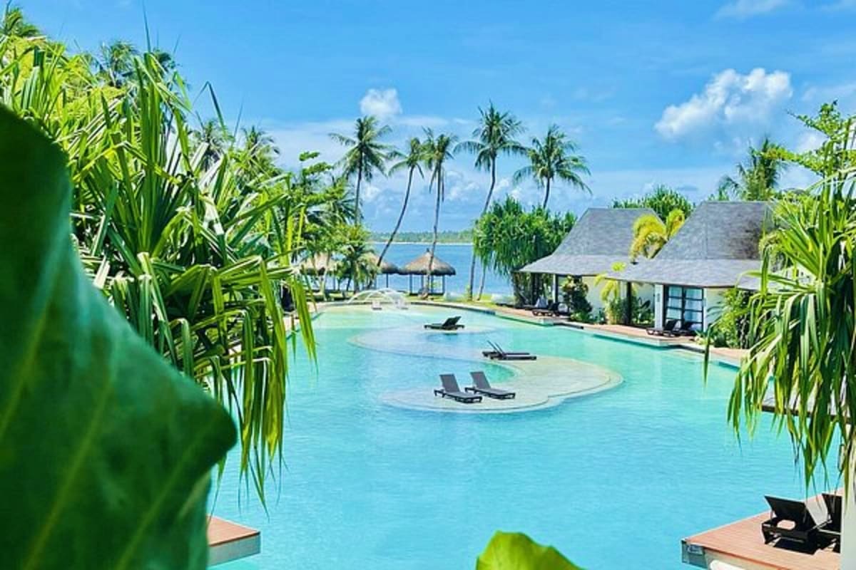 Tropical beach resort with turquoise lagoon pool, palm trees, thatched bungalows, and ocean view at Simply Siargao