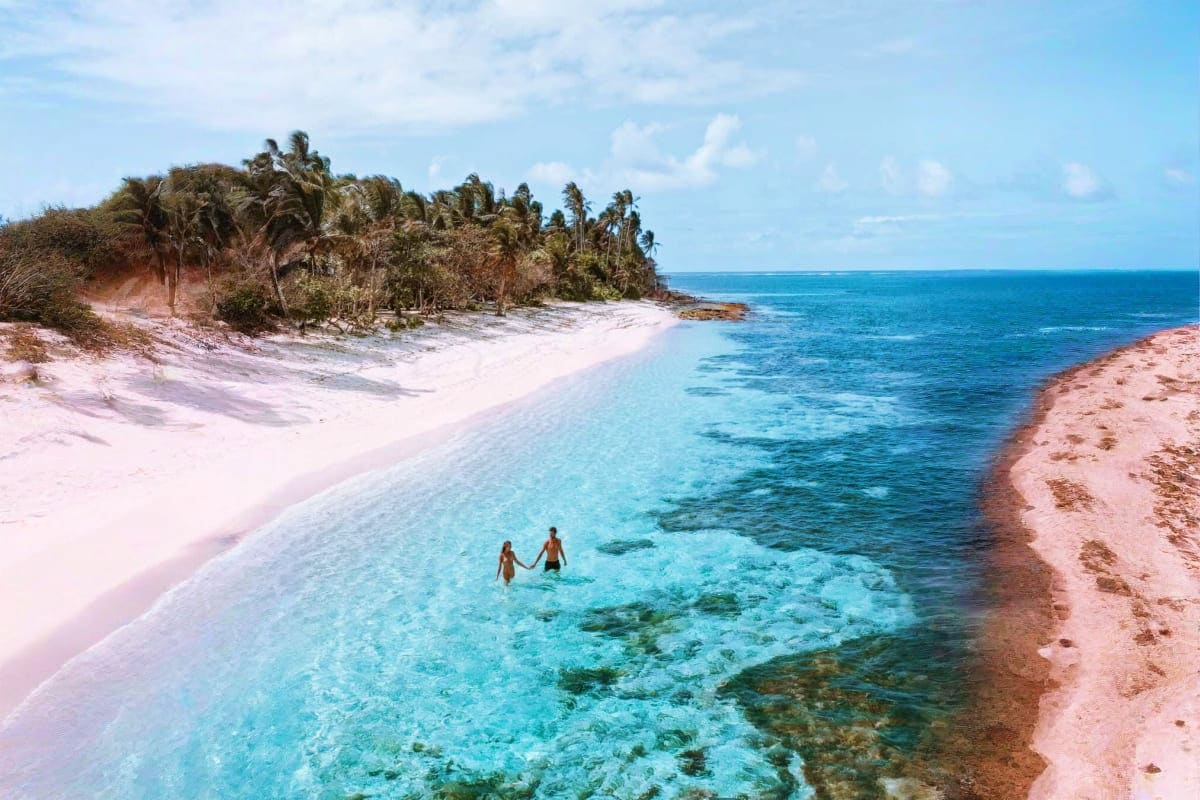Simply Siargao Two swimmers in turquoise waters off pink sand beach with palm trees and rocky coastline at Siargao Island