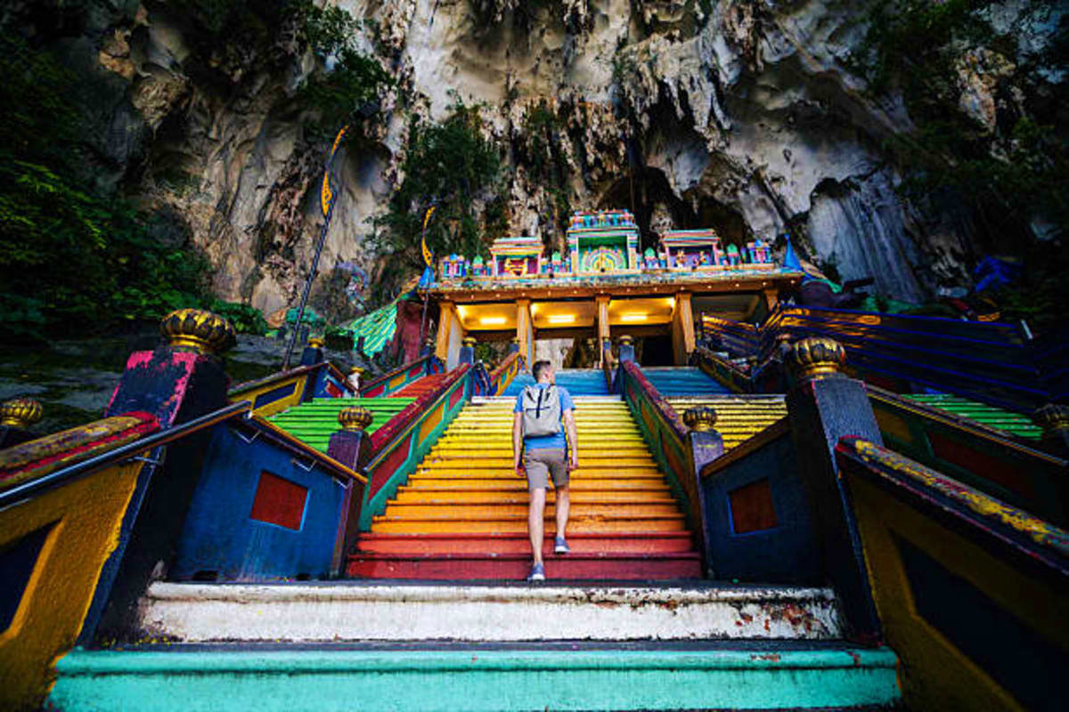 Tourist climbing colorful rainbow steps toward ornate temple shrine in limestone cave at Batu Caves, Malaysia