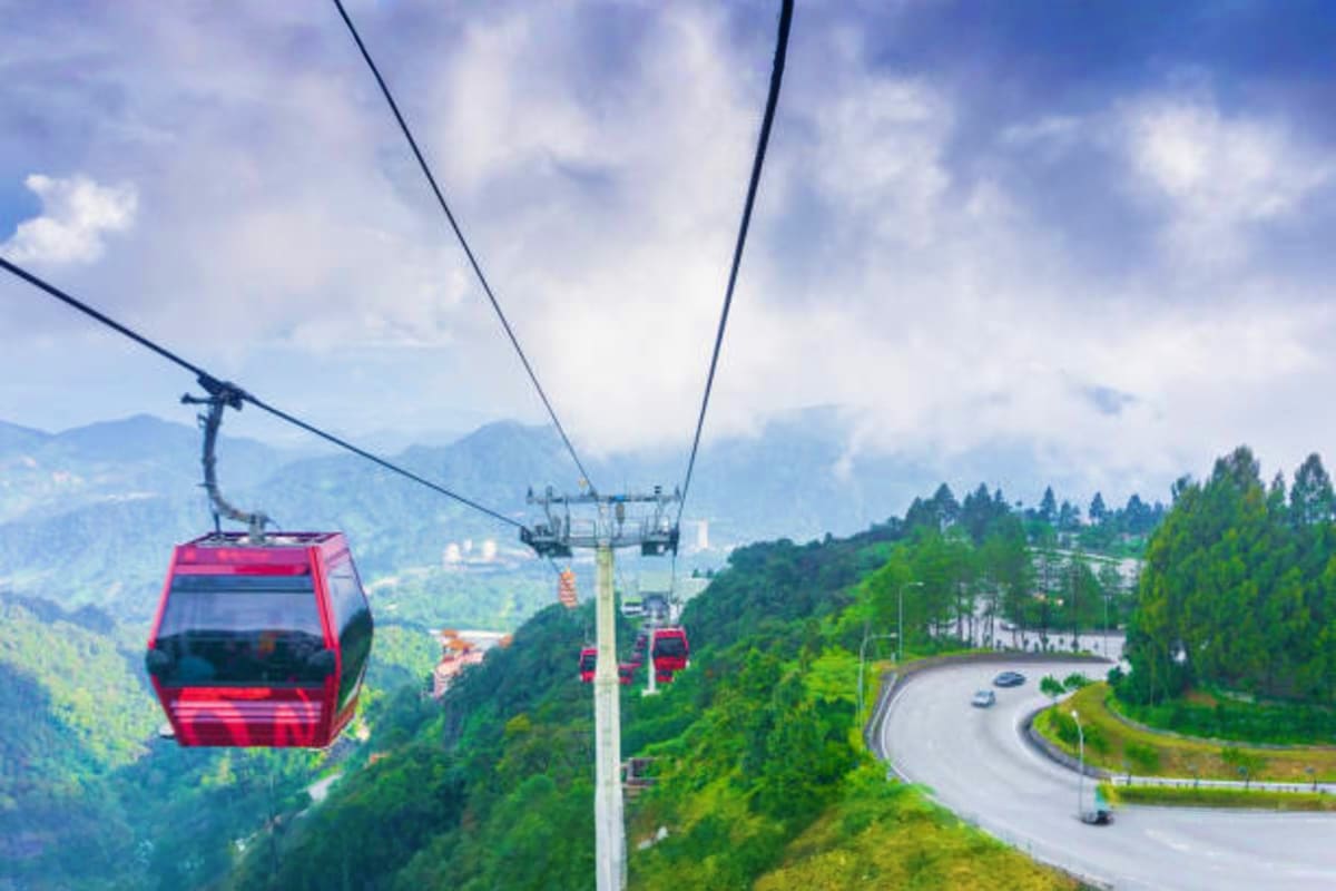 Red cable car suspended over mountainous terrain with forested hills and winding road below in Malaysia