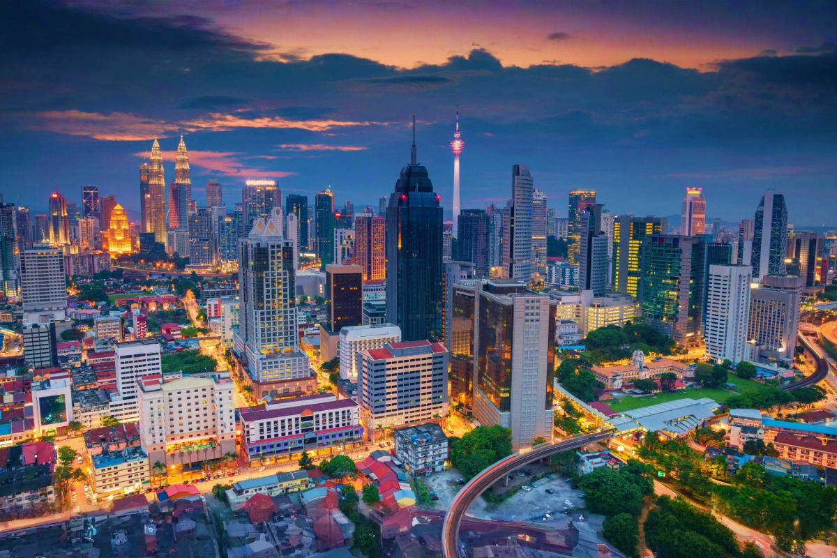 Kuala Lumpur skyline at twilight with illuminated Petronas Twin Towers and Menara Tower against sunset sky