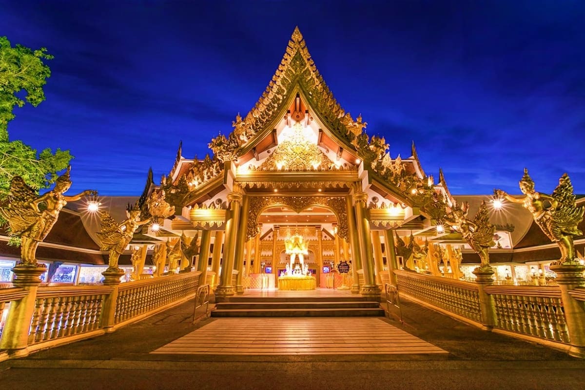 Illuminated Thai Buddhist temple at night with ornate golden spires, detailed architecture, and traditional dragon statues fl