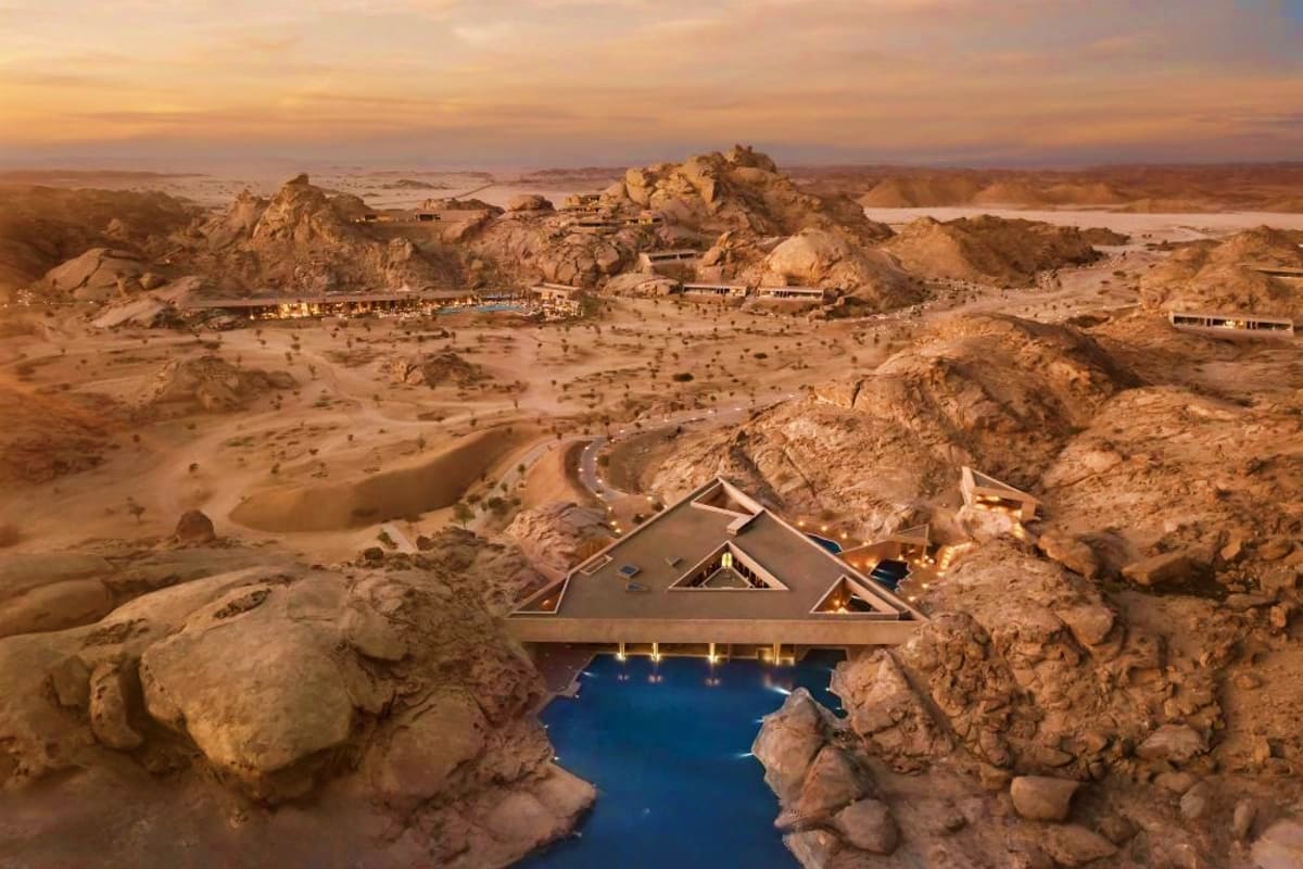 Luxury resort built into desert rocks overlooking a blue pool and expansive arid landscape at sunset in the Red Sea region