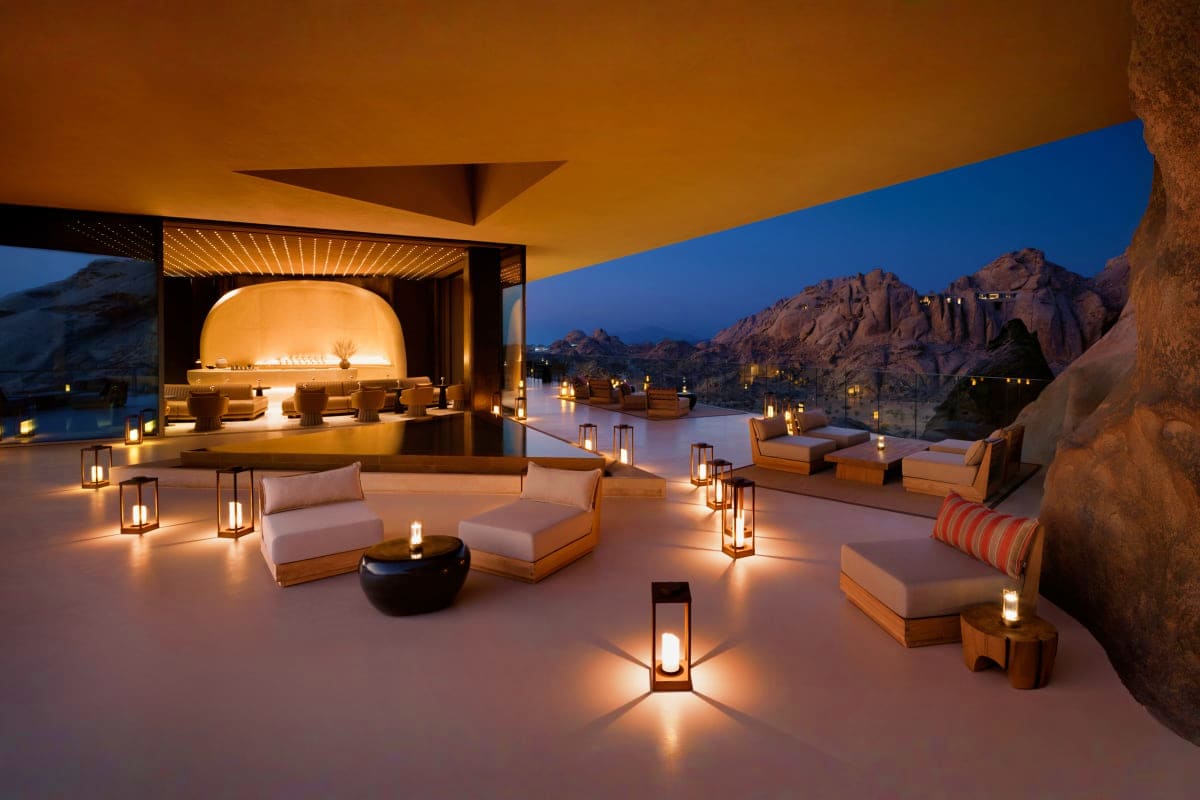 Luxury resort terrace at dusk with modern seating, glowing lanterns, and rocky desert mountains in the background overlooking