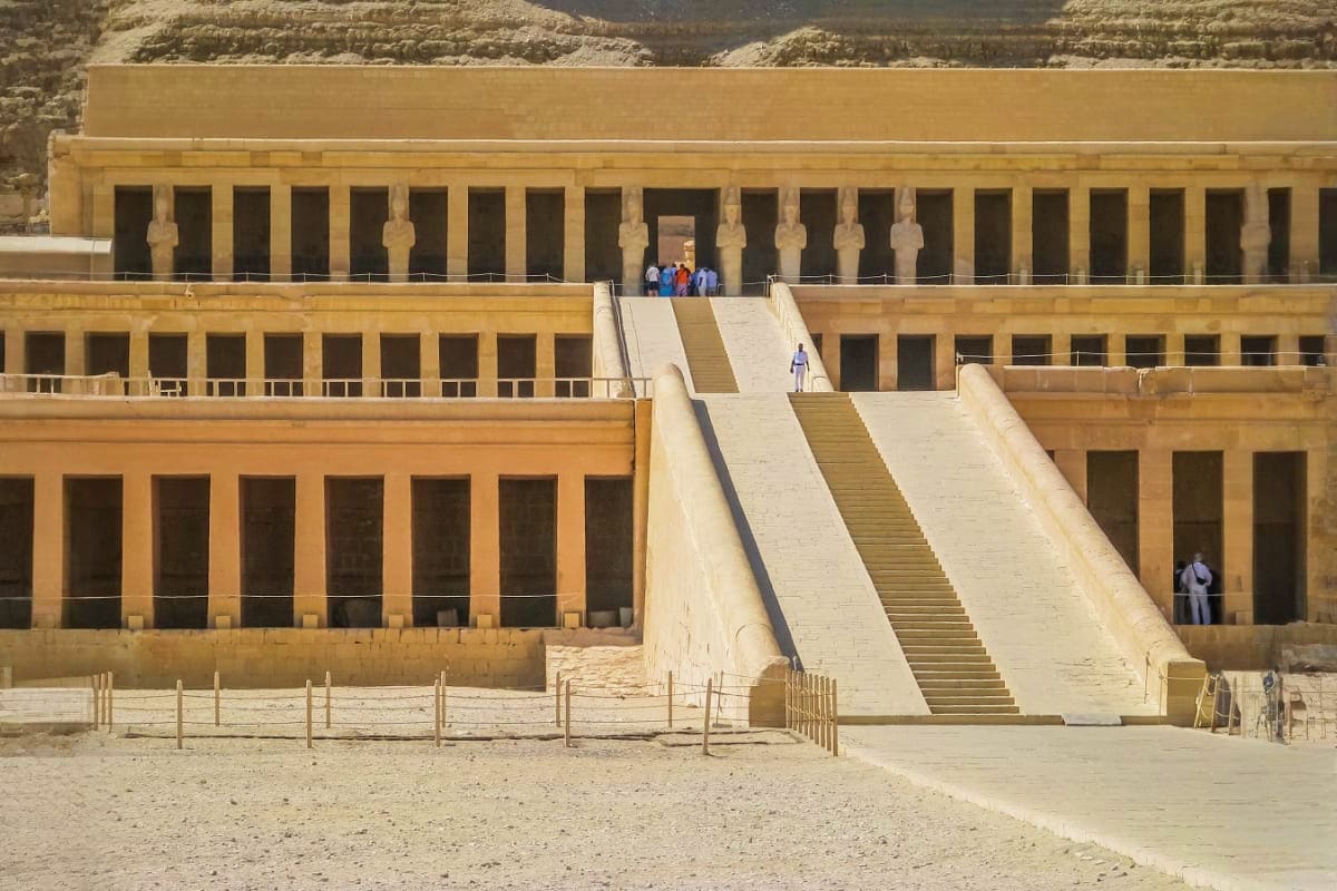 Temple of Hatshepsut in Luxor, Egypt with grand stone colonnade and central ramp staircase, tourists on upper terrace.