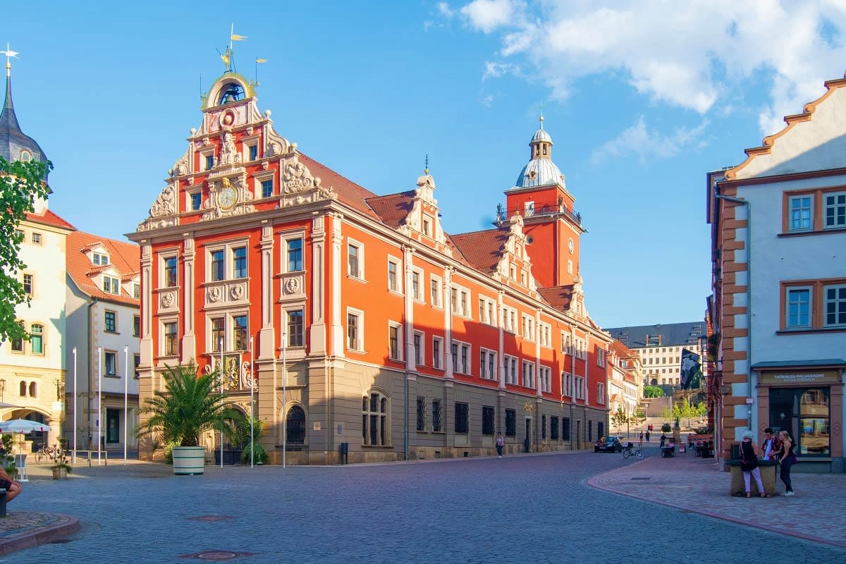 Historic red town hall with ornate clock tower and spires in a German city square on a sunny day