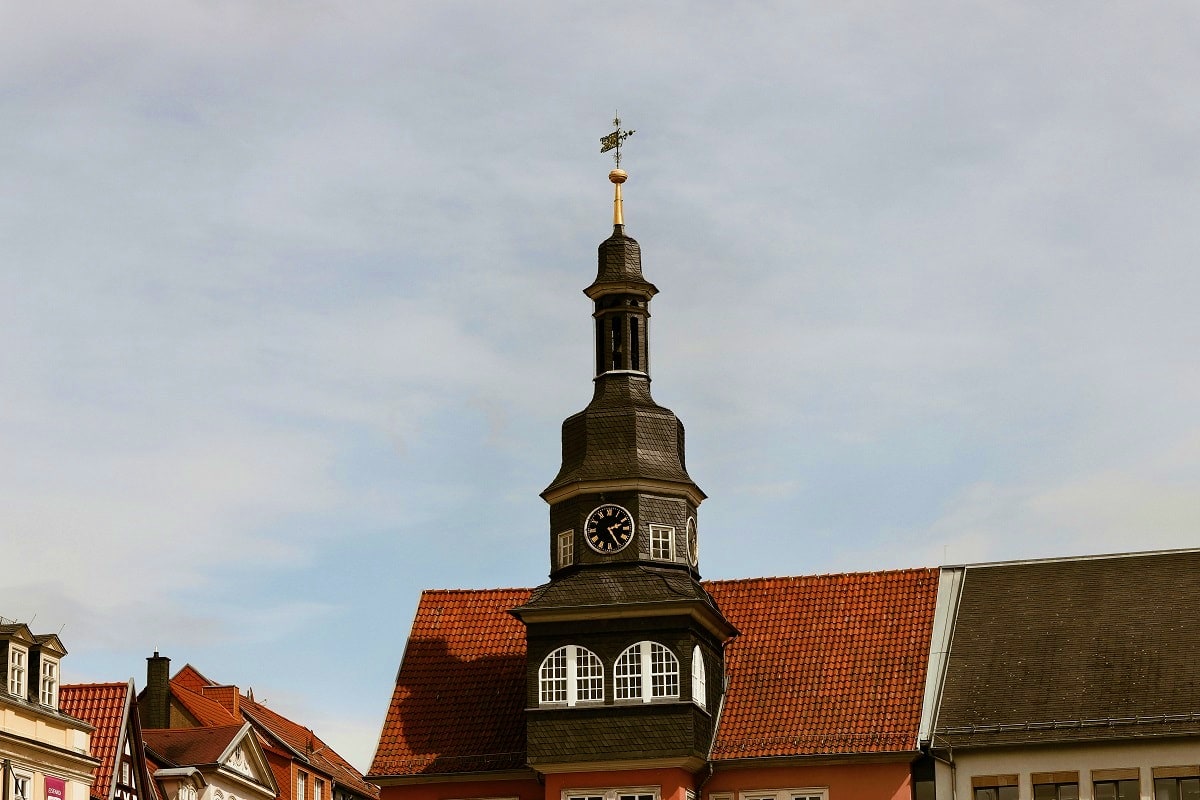 Historic church clock tower with dark wooden spire and cross, set among traditional German buildings with red tile roofs