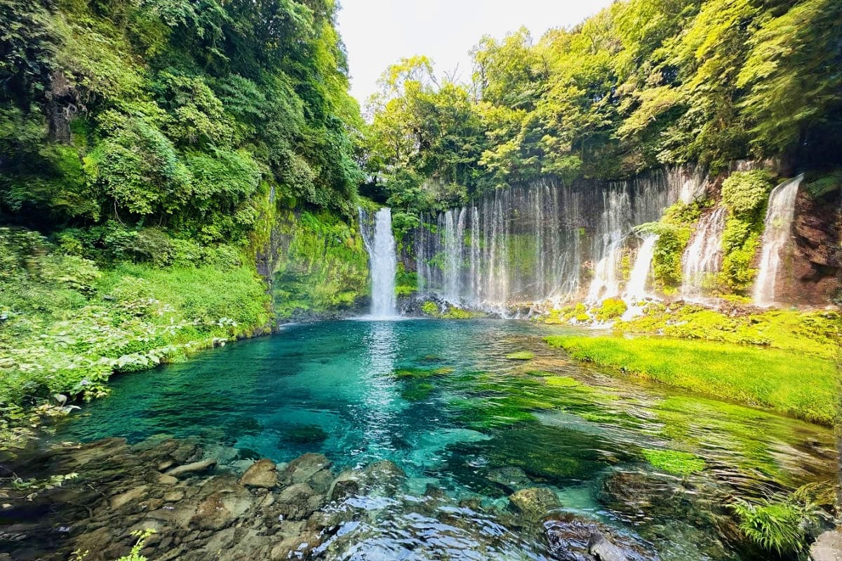 Shiraito Falls waterfall in lush green forest with turquoise pool and moss-covered basalt cliffs in Japan