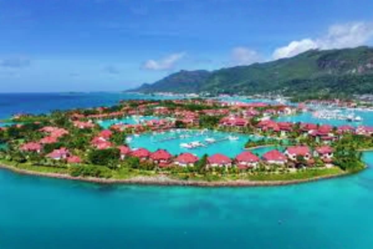 Aerial view of tropical island resort with red-roofed villas, turquoise lagoons, and lush green mountains in Seychelles