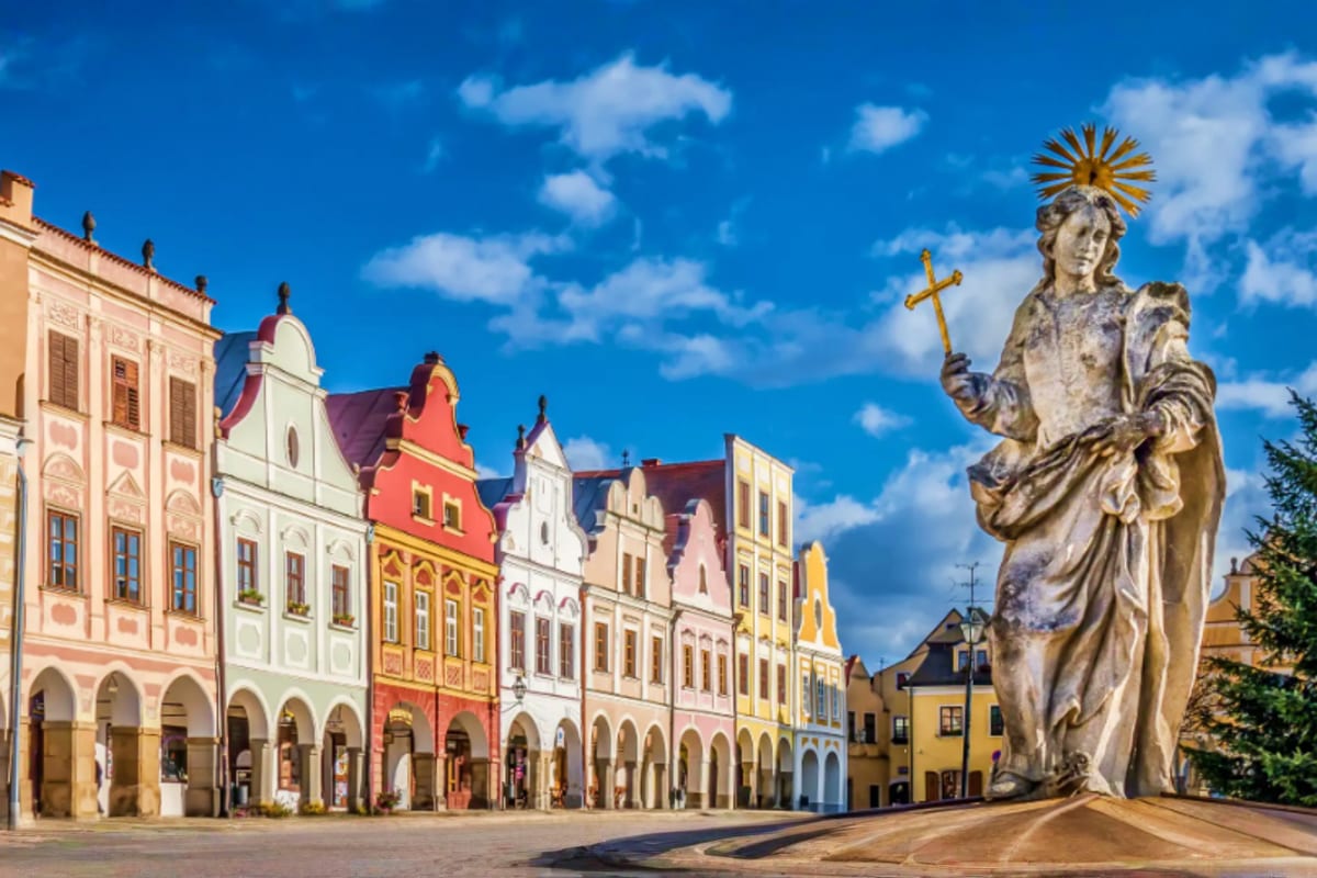 Historic town square in Czech Republic featuring colorful Renaissance buildings and stone statue of saint with golden halo an