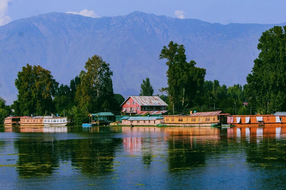 Colorful houseboats and waterfront homes reflected in still water with snow-capped mountains and poplar trees in Kashmir vall