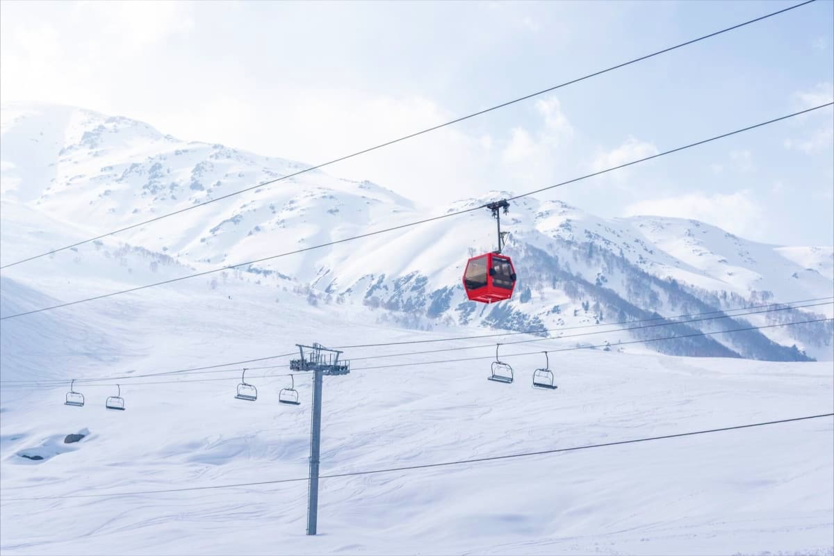 Magical Kashmir Retreat Lakes Gardens and Snow Red gondola cable car ascending snowy mountain slope with ski lift chairs and snow-covered peaks in background