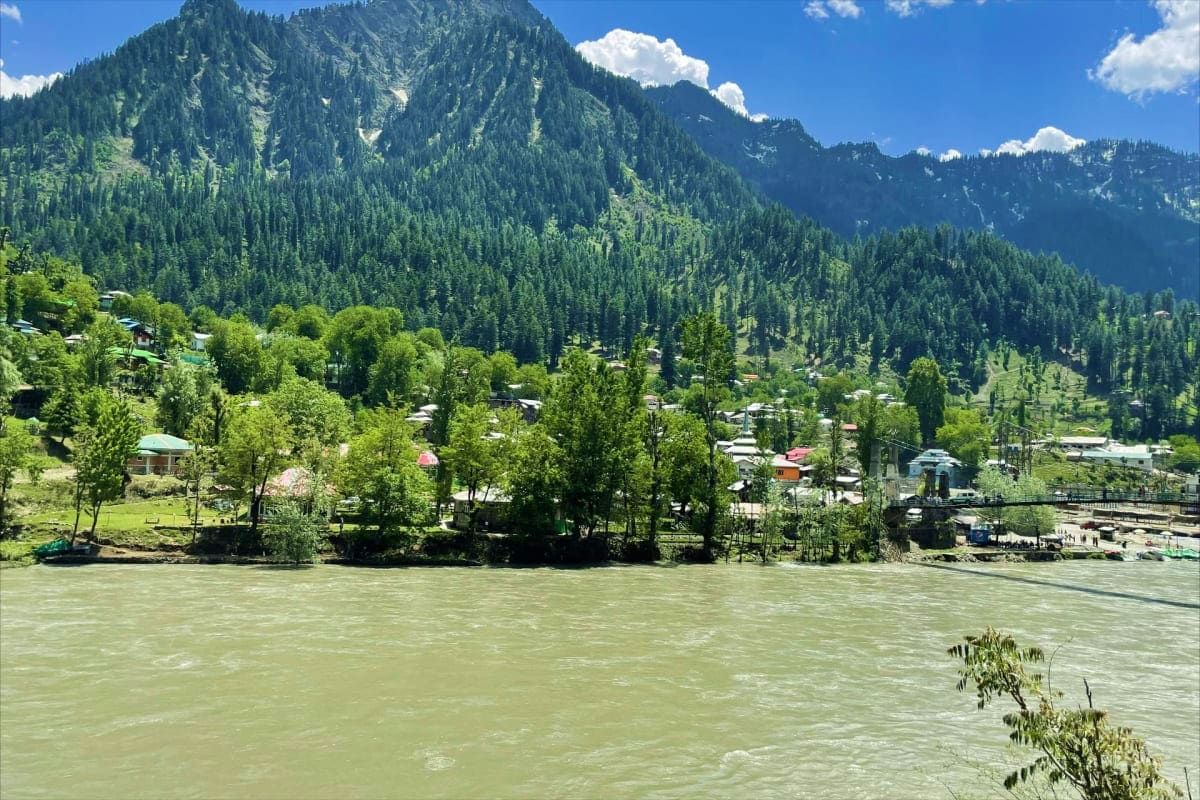 Magical Kashmir Retreat Lakes Gardens and Snow Turquoise river flowing through a forested valley with snow-capped mountains, traditional houses nestled among tall pine tree