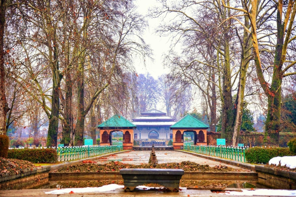 Symmetrical garden pavilion with turquoise roof flanked by bare trees and formal hedge-lined pathways in winter