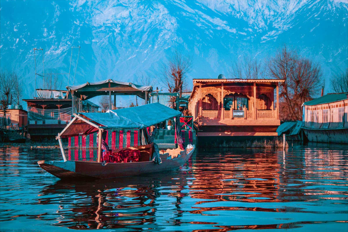 Traditional wooden houseboat with red striped cabin on Dal Lake in Srinagar, Kashmir, with snow-capped mountains and houseboa