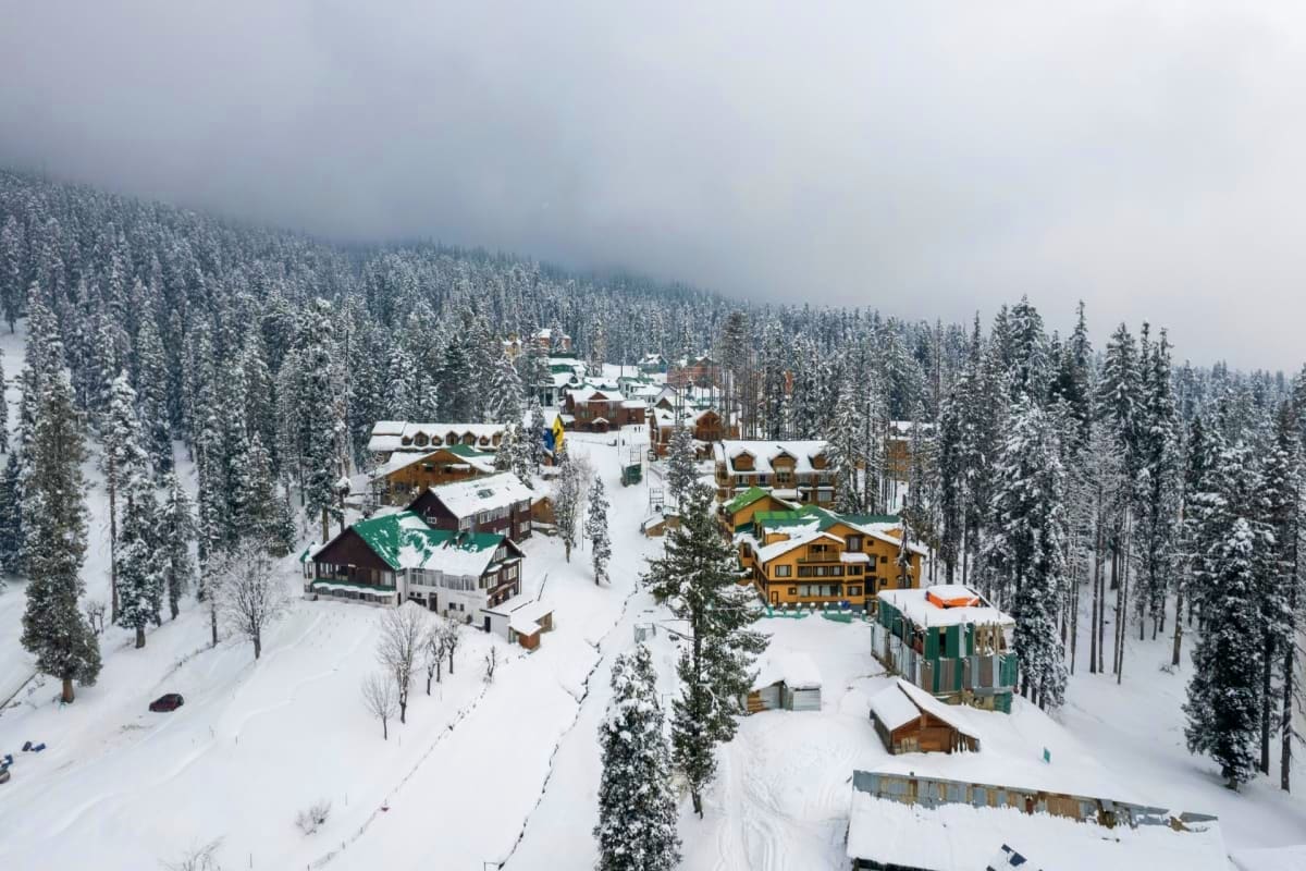 Kashmir Joyful Family Tour Lakes Gardens and Snow Adventures Aerial view of a snow-covered mountain resort surrounded by evergreen forests and wooden lodges in Kashmir