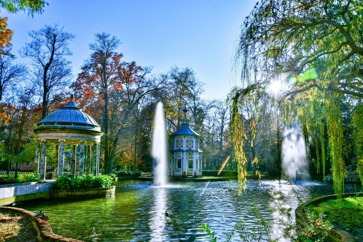 Classic European palace garden with ornate blue domed gazebos, fountains, weeping willow trees, and serene pond landscape