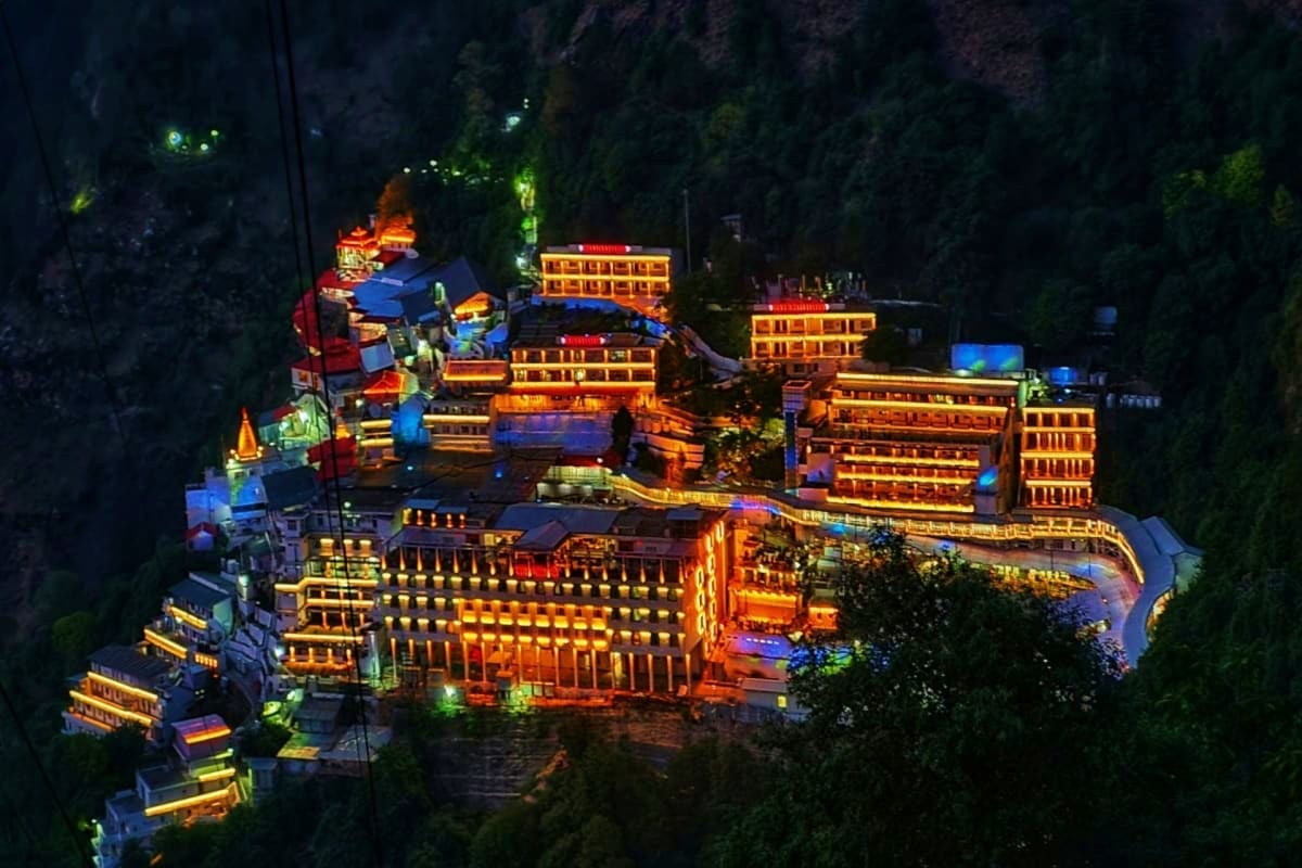 Aerial night view of illuminated temple complex nestled in forested mountains with golden-lit buildings and structures