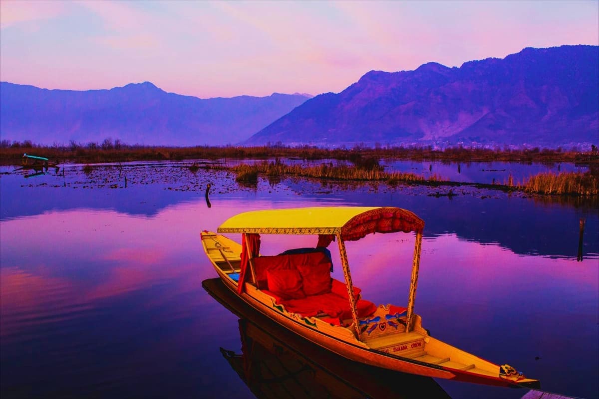 Traditional yellow and red boat with canopy anchored in calm purple waters at sunset with snow-capped mountains and wetlands 