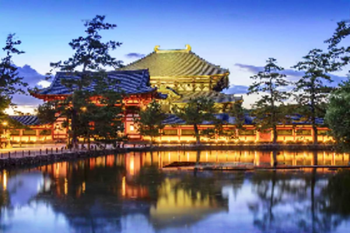 Illuminated traditional Japanese temple with golden roof reflected in still water at dusk, surrounded by evergreen trees