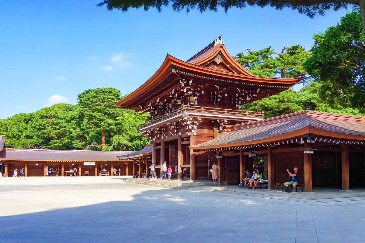 Classic Japan Trio Traditional Japanese temple with curved orange roof and wooden architecture surrounded by lush green trees, visitors in court