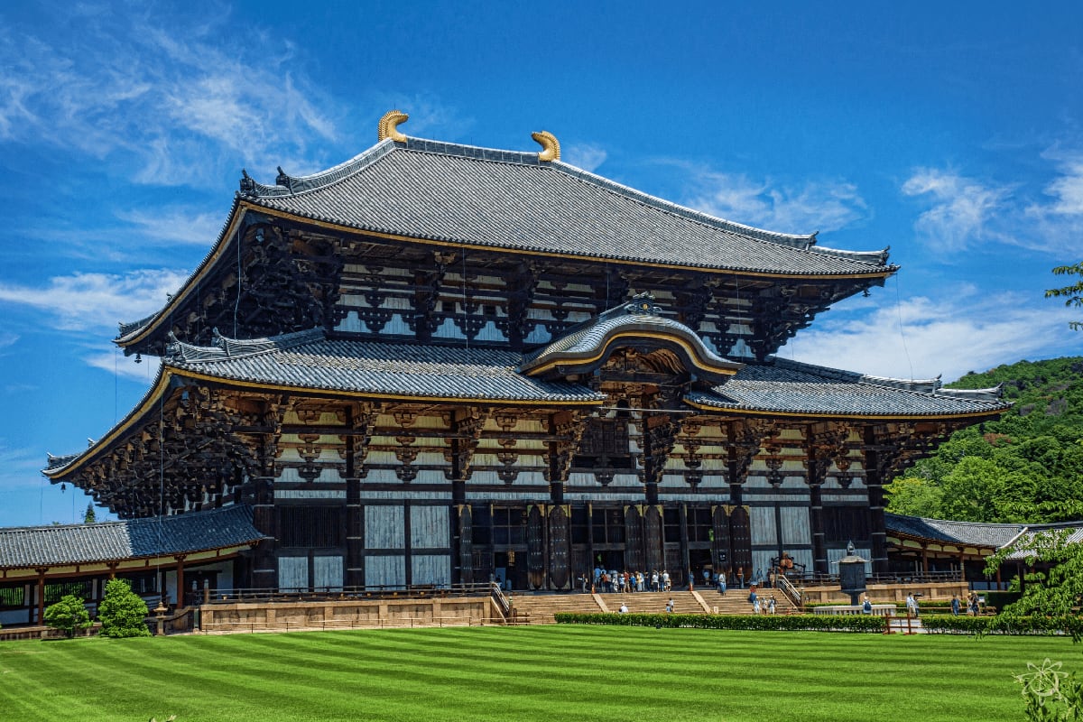 Todai-ji Temple's Great Buddha Hall in Nara, Japan, with traditional curved roofs and golden ornaments against blue sky
