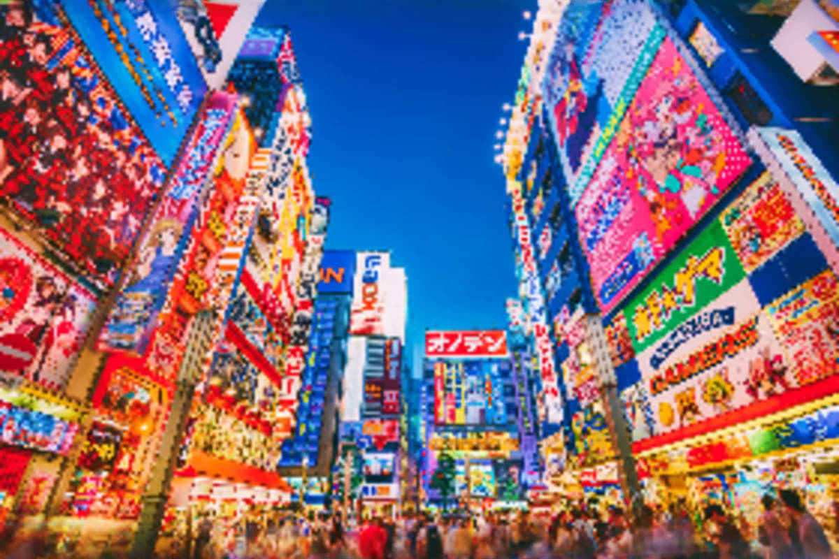 Vibrant street in Tokyo's Shibuya district decorated with colorful neon signs and crowded with pedestrians under blue sky