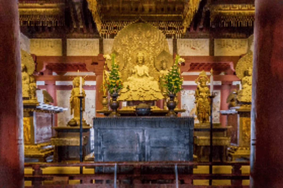 Golden Buddha statue in ornate Thai temple shrine with red and gold architecture, green floral arrangements, and traditional 