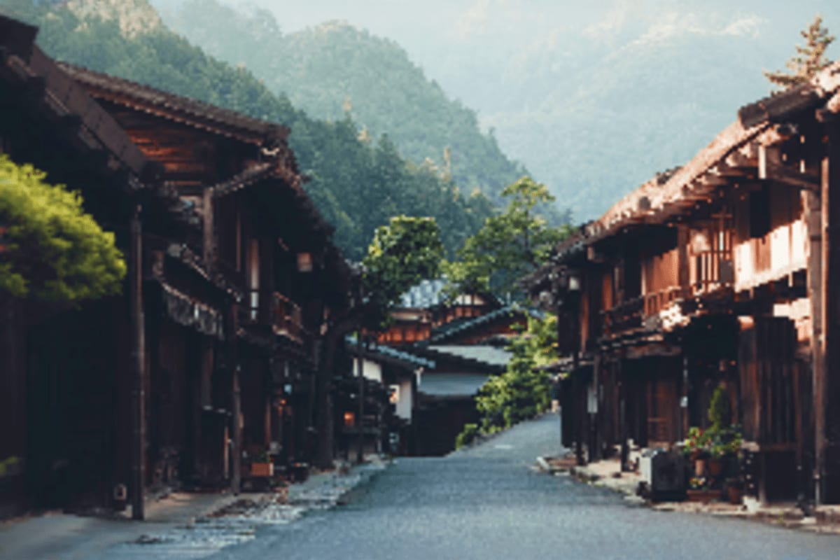 Traditional wooden houses with curved roofs lining a peaceful street in a misty mountain valley, representing classic Japanes