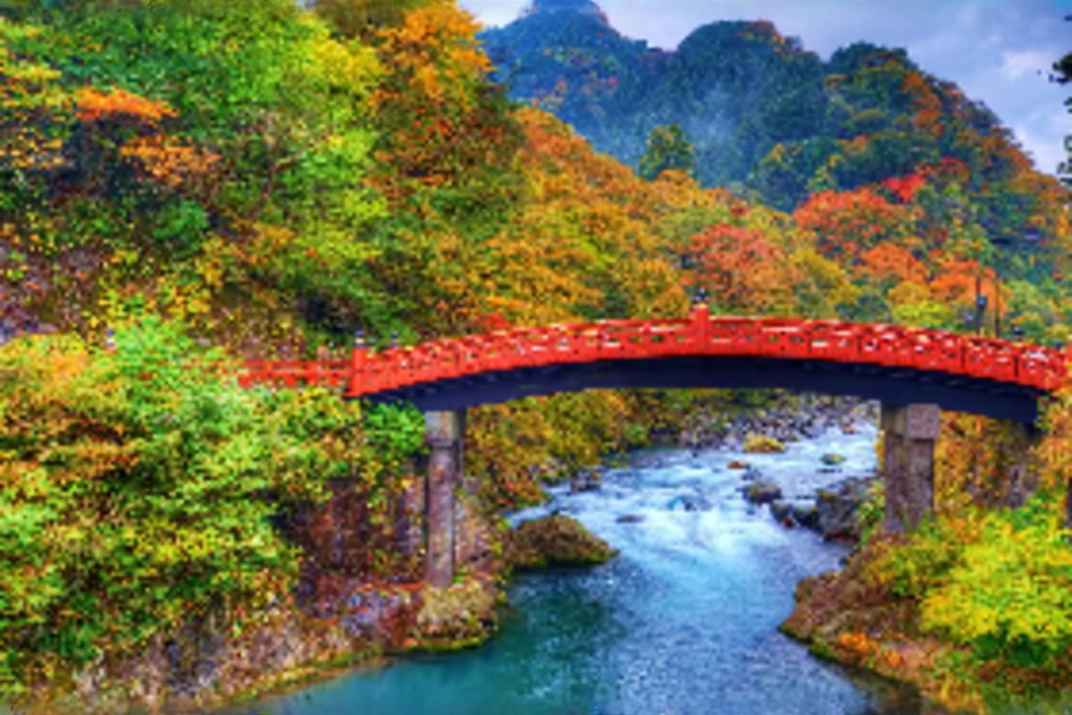 Red arched bridge spanning blue river with autumn foliage and mountains in background, Nikko Japan scenic landscape