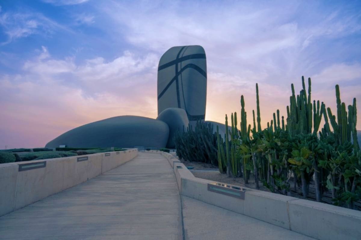 Modern architectural structure with tall pipe sculpture overlooking desert landscape with organ pipe cacti and paved walkway 