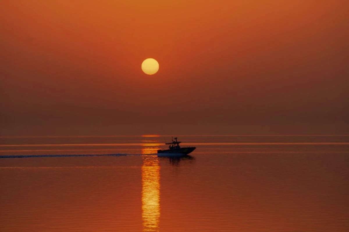 Silhouette of a fishing boat on calm water at sunset with golden sun reflecting on the sea surface against an orange sky
