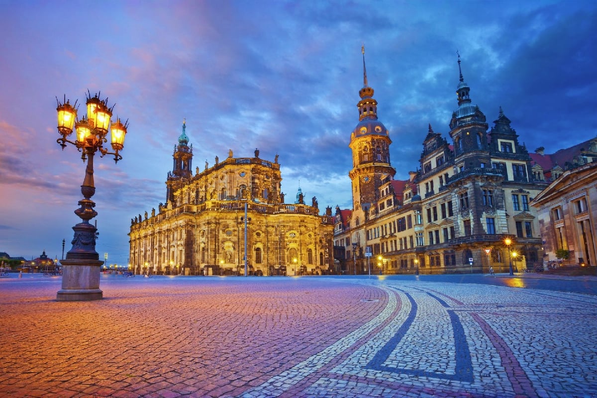 Historic German square at dusk with illuminated baroque church, ornate lamp post, and classical buildings under blue evening 