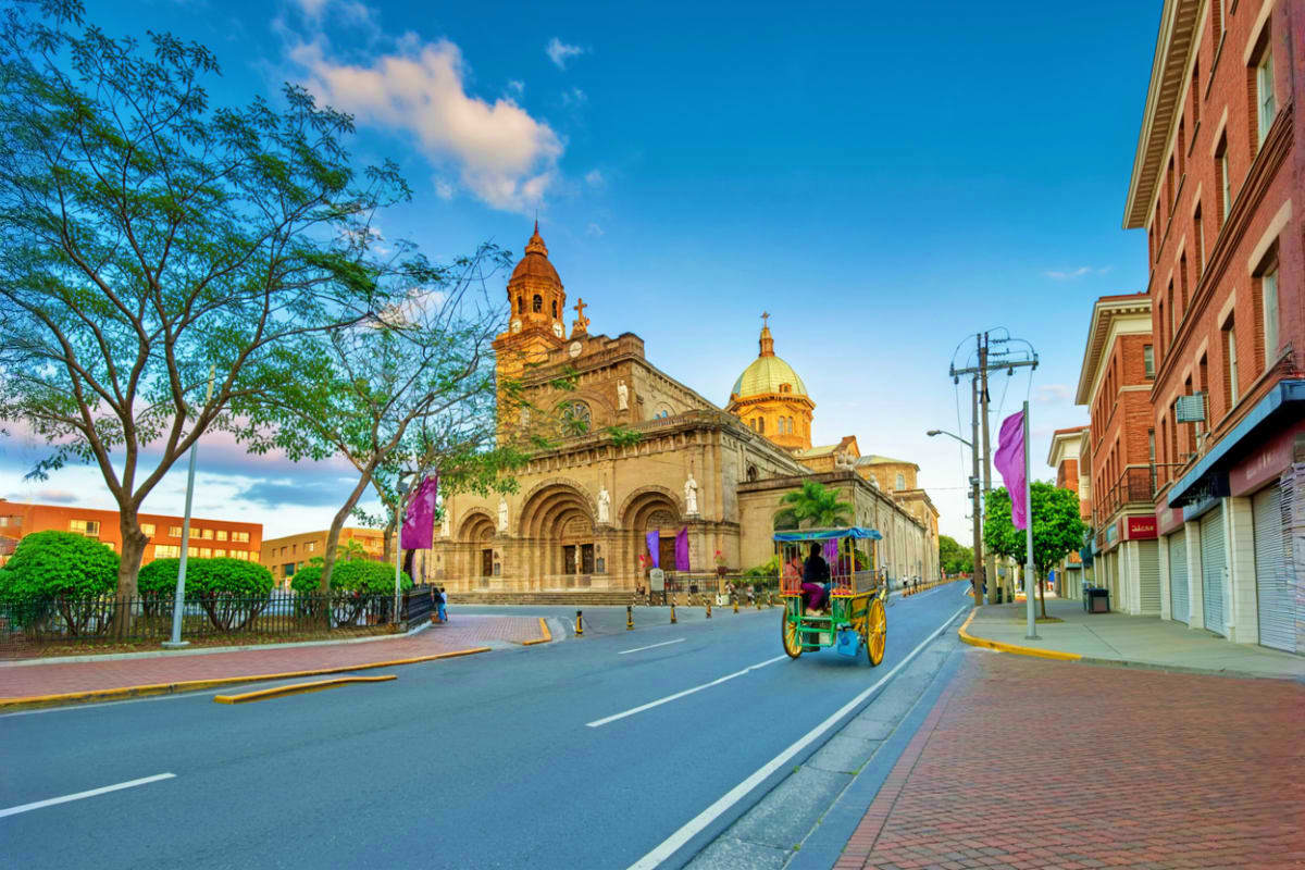 Explore Manila And Cebu at Your Own Pace Colorful horse-drawn carriage passing historic colonial cathedral with golden domes on street in Philippine city center