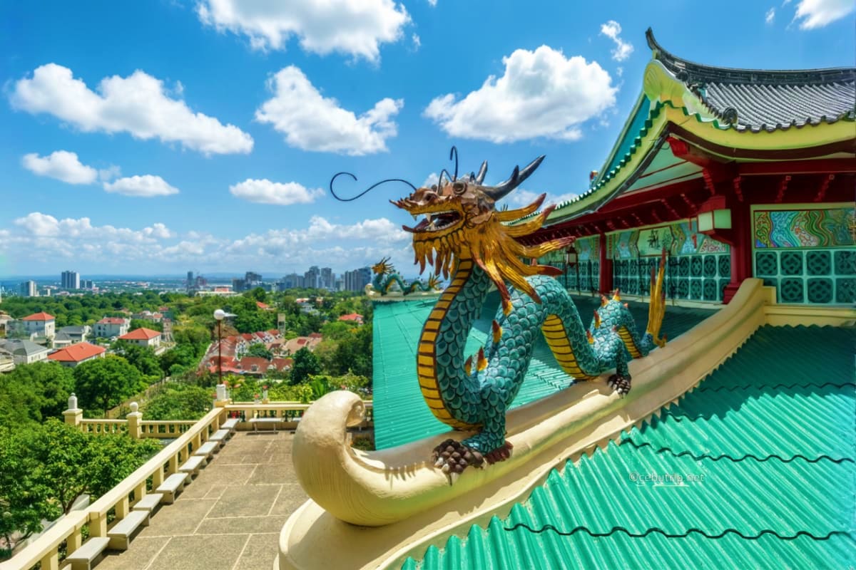 Explore Manila And Cebu at Your Own Pace Ornate dragon statue on turquoise-roofed Asian temple overlooking Manila cityscape and green landscape under blue sky