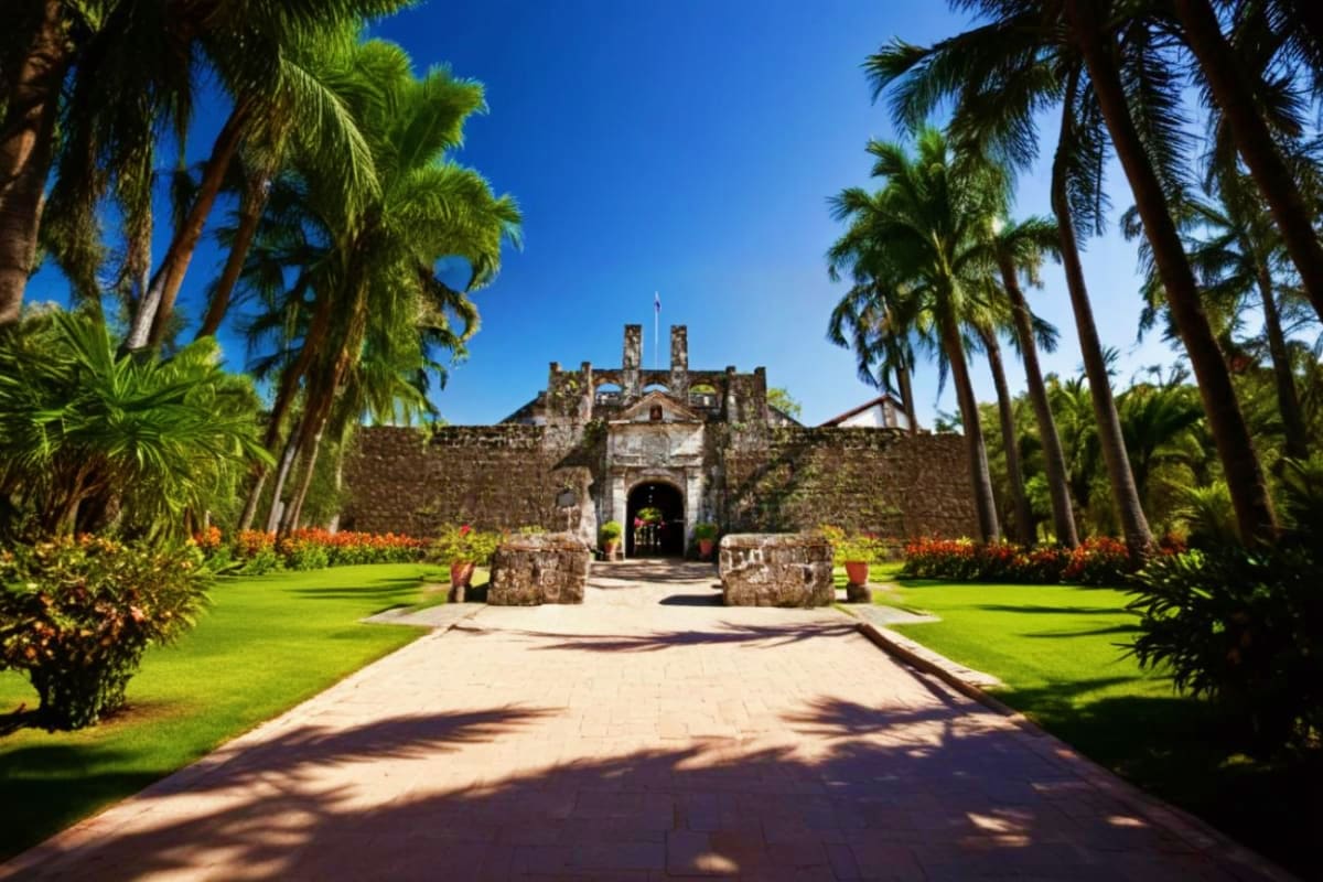 Explore Manila And Cebu at Your Own Pace Historic stone fortress with palm tree-lined entrance pathway and manicured gardens under clear blue sky in Philippines
