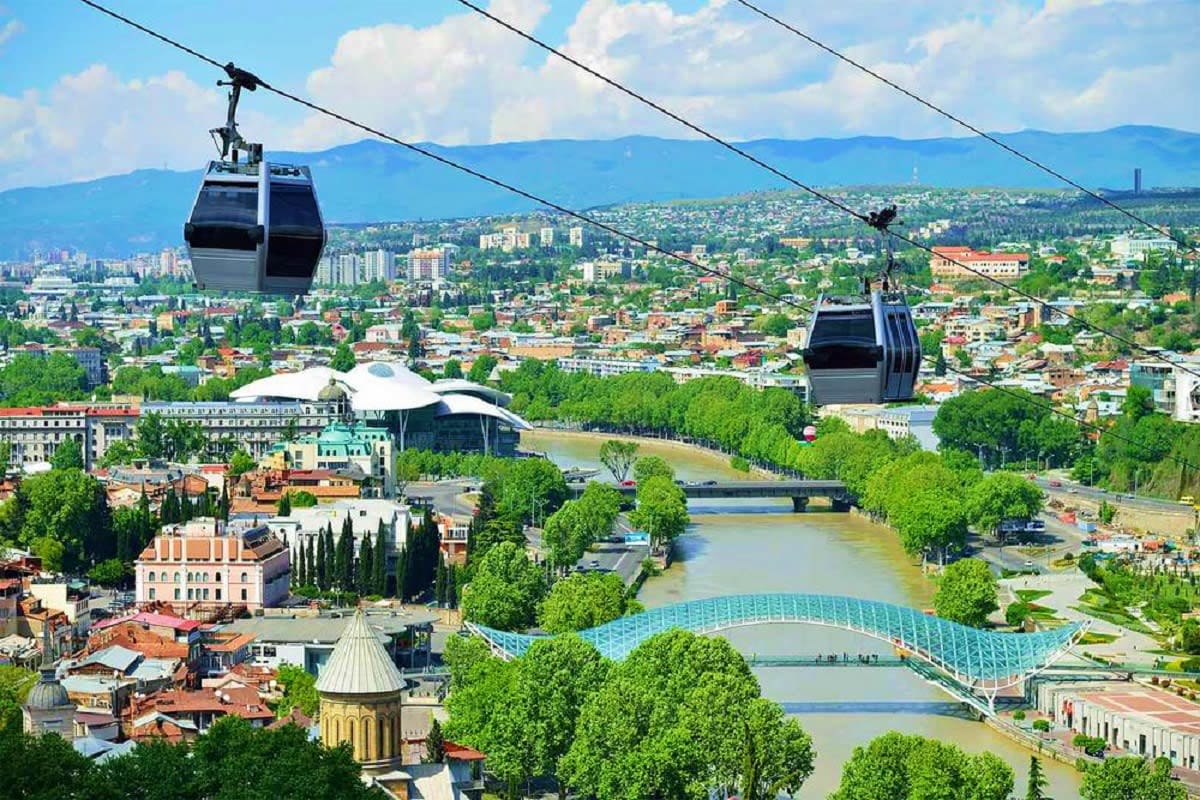 Aerial view of Tbilisi with cable car cabins, Metekhi Church, Mtkvari River, and mountain backdrop in Georgia