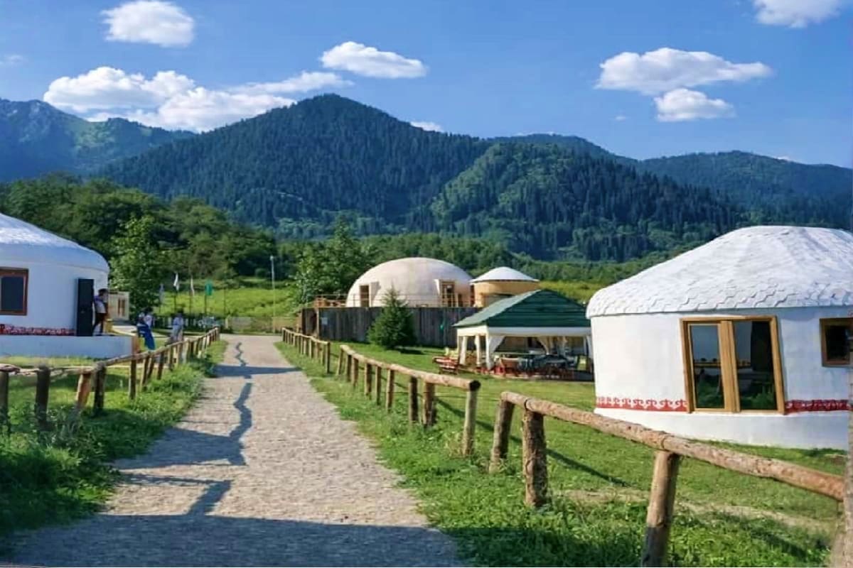 Yurt accommodations and traditional dome structures in a mountain valley with forested peaks and green meadows in Kazakhstan