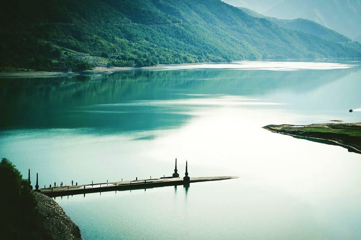 Eternal Romance in Georgia Long wooden pier with twin spires extending into turquoise glacial lake surrounded by forested mountains in Georgia