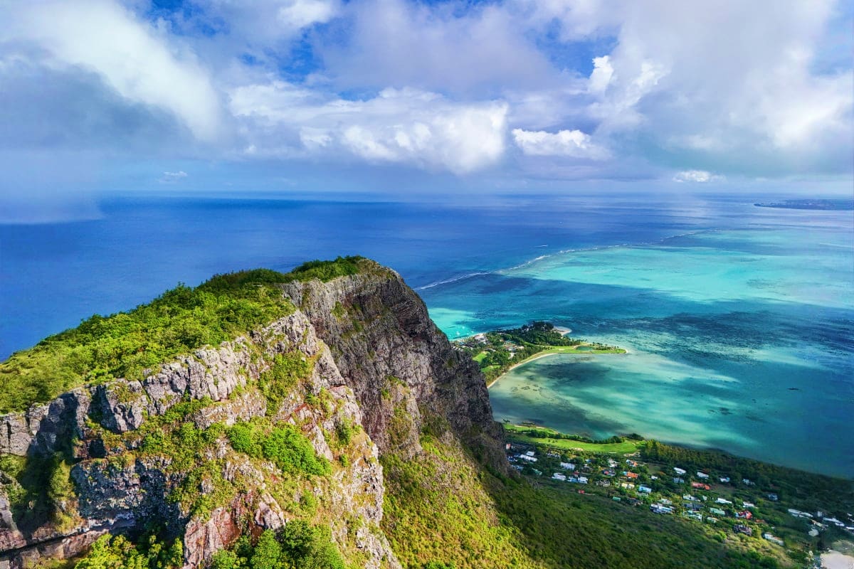 Mauritius Royal Escape Aerial view of rocky cliff with turquoise lagoon, coral reef, and coastal village in Mauritius