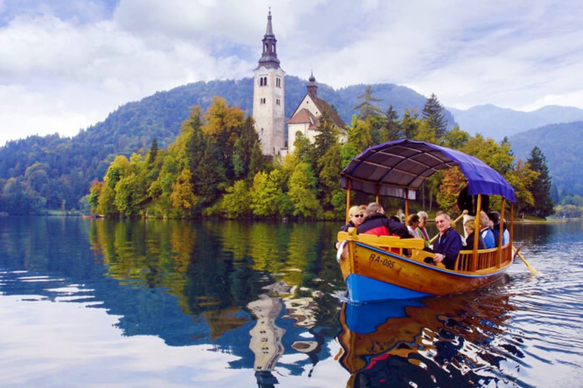 Traditional wooden boat with tourists on Lake Bled, Slovenia, with Church of the Mother of God and forested mountains in back