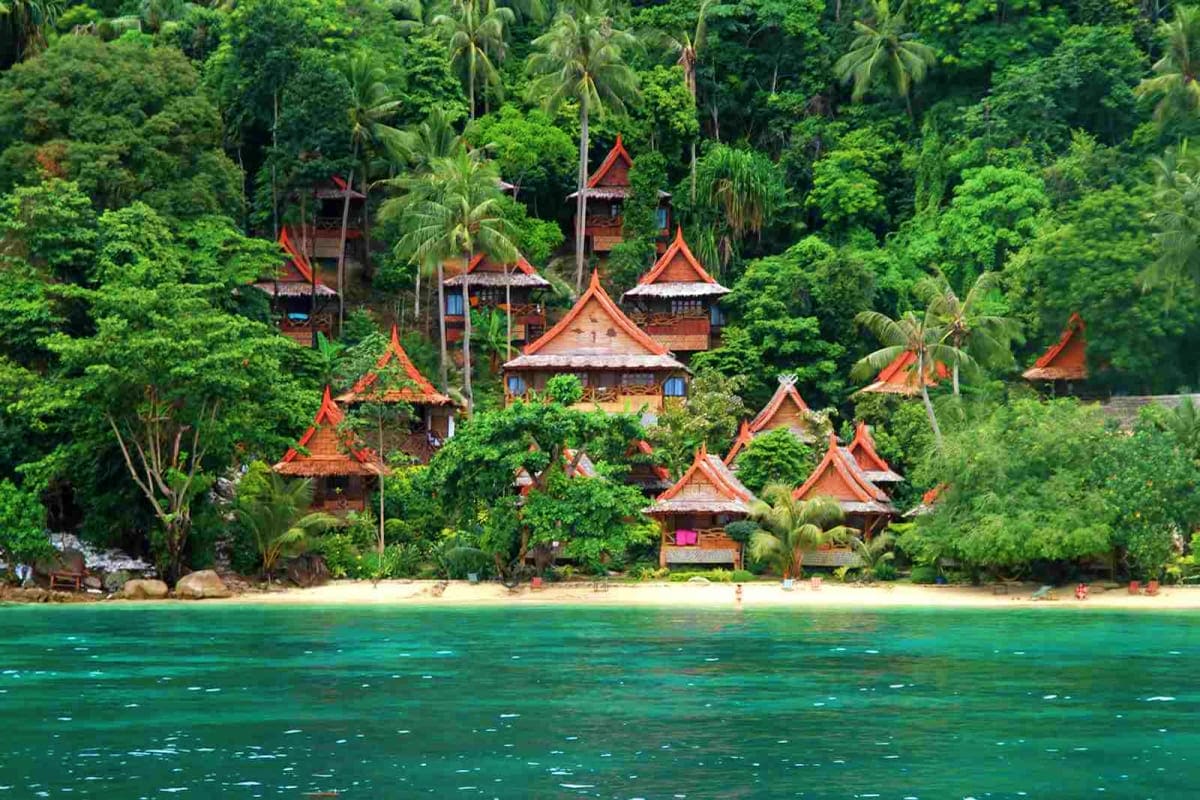 Exclusive Phuket Holidays Traditional Thai temple buildings with red-orange roofs nestled in lush jungle vegetation along a turquoise tropical beach in